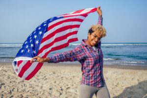 happy afro american woman holding usa flag at sunny tropical beach